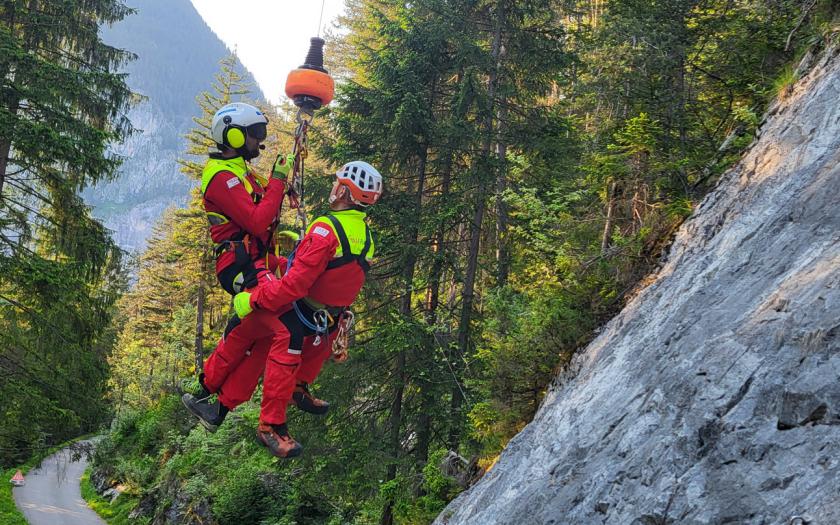 Zwei Personen hängen an der Rettungswinde neben einem Berghang in einem Tal