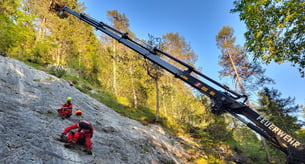 Ein Kran, an dem zwei Personen an einer Rettungswinde hängen, ist über einen Berghang ausgefahren.
