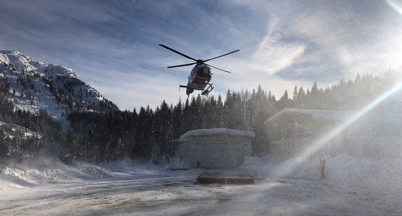 Ein rot-weißer Hubschrauber steigt in die Luft und wirbelt dabei Schnee auf
