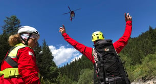 Ein Bergretter gibt einem in der Luft schwebenden Rettungshubschrauber ein Handzeichen 